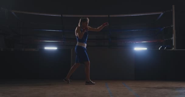 Een mooie vrouw voert een strijd van de schaduw tijdens het beoefenen van hard voor toekomstige overwinningen. Donkere sportschool achtergrond. Steadicam schot — Stockvideo