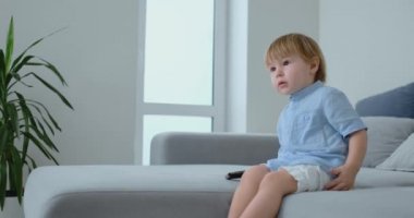 2 yaşında erkek bir koltukta oturur ve onun elinde uzaktan kumanda ile otururken Tv izliyor. Çizgi film ve Tv şovları Çocuklukta görüntülemek