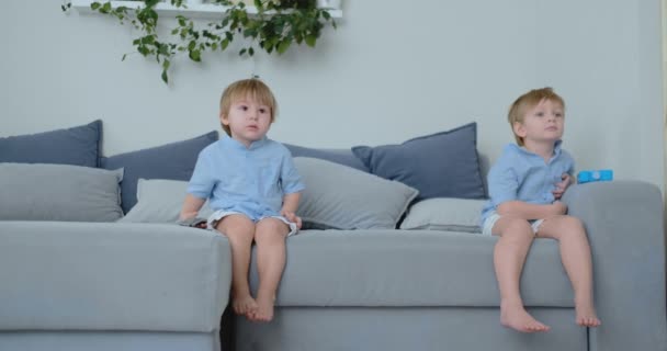 Дети смотрят телевизор. Маленькие дети сидят на диване и смотрят мультики — стоковое видео