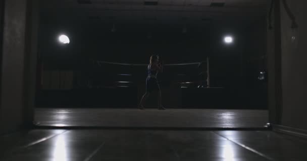 Prachtige vrouwelijke bokser otbryvatyvat klappen voert een strijd met schaduw in een donkere hall van de hall in slow motion in blauwe kleding en rode pleisters op haar polsen. zoomcamera. Steadicam — Stockvideo