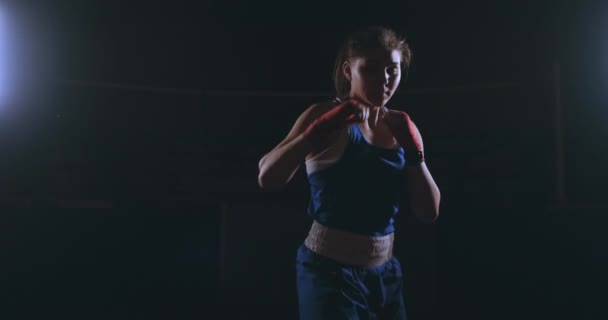 Mooie sexy vrouw bokser strikes dynamisch rechtstreeks in de camera en vooruit zich beweegt op een donkere achtergrond met een backlight. Camera beweegt Steadicam schot — Stockvideo