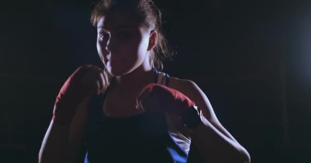 Güzel bir kadın boksör kameraya bakarak bir arkadan aydınlatmalı ışık ile karanlık bir arka plan iş başında. Steadicam atış — Stok video