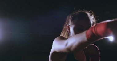 Güzel seksi kadın boksör dinamik olarak bir arka ışık ile karanlık bir arka plan üzerinde doğrudan içine belgili tanımlık fotoğraf makinesi ve hareketli ileri geliyor. Kamera Steadicam atış taşır