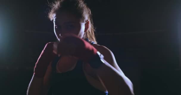 Tittar in i kameran en vacker kvinnlig boxare slår mot en mörk bakgrund med en bakgrundsbelyst ljus. Steadicam skott — Stockvideo