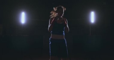 Güzel bir kadın boksör kameraya bakarak bir arkadan aydınlatmalı ışık ile karanlık bir arka plan iş başında. Steadicam atış