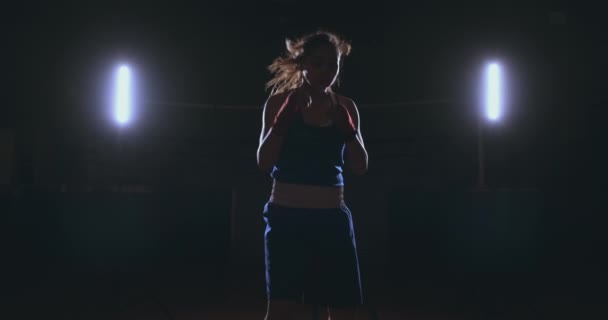 Op zoek naar de camera een mooie vrouwelijke bokser stakingen tegen een donkere achtergrond met een licht verlicht. Steadicam schot — Stockvideo