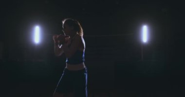 Elleri ve mavi tişört üzerinde kırmızı bandaj güzel spor boxer kadında hızı ve tekniği yumruklar pratik bir gölge ile mücadele ediyor. Kamera hareketi yan görünümü. Steadicam atış