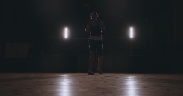 Opleiding een mooie vrouwelijke bokser stoten in een donkere kamer doen. Steadicam geschoten. Voorbereiding voor zelfverdediging en strijd in de ring — Stockvideo