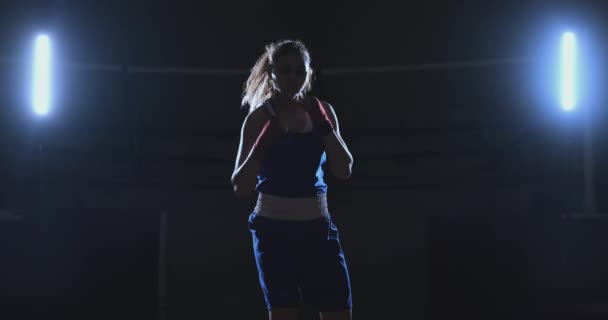 Eine schöne Sportboxerin mit roten Binden an den Händen und einem blauen T-Shirt kämpft mit einem Schatten, der die Geschwindigkeit und Technik der Schläge übt. Kamerabewegung Seitenansicht. Steadicam-Aufnahme — Stockvideo