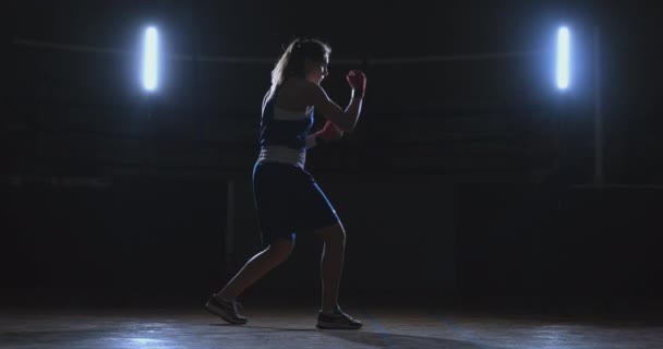 Training einer schönen Boxerin, die in einem dunklen Raum Schläge macht. Steadicam-Aufnahme. Vorbereitung auf Selbstverteidigung und Kampf im Ring — Stockvideo