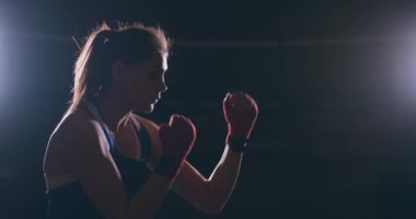 Elleri ve mavi tişört üzerinde kırmızı bandaj güzel spor boxer kadında hızı ve tekniği yumruklar pratik bir gölge ile mücadele ediyor. Kamera hareketi yan görünümü. Steadicam atış