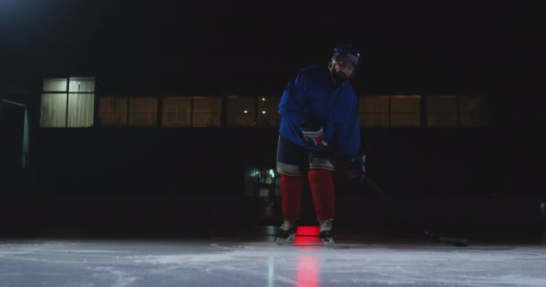Muž hokejista s PUK na ledě v podobě hokej listy s holí v ruce ze tmy a dívá se přímo do kamery
