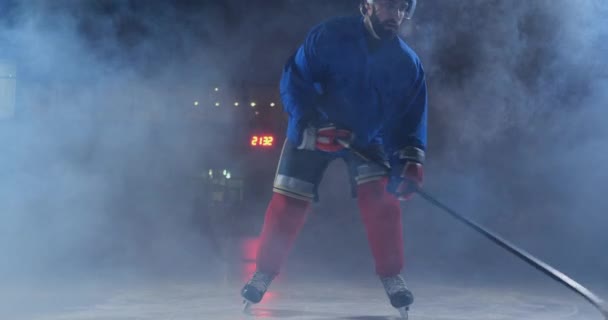 Profesionální hokejista s holí a PUK se pohybuje na Luda na brusle a helmu na tmavém pozadí a kouř. Dribling s pukem mladého muže v ice Areně