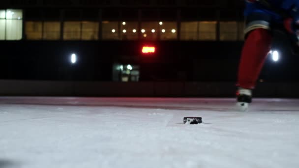 Il primo piano del disco è sul ghiaccio e nel giocatore di hockey al rallentatore si avvicina e la neve vola nella fotocamera e lui prende il bastone del disco — Video Stock