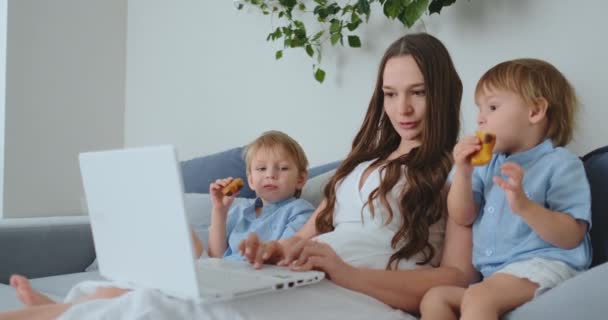 Vacker ung mamma och två små barn pojkar tittar på laptop skärmen familjefoton. Och göra online shopping — Stockvideo