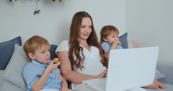 Gyönyörű fiatal anya és a két kis gyerekek fiú keres a laptop képernyő családi fotók. És mégis, online vásárlás. Nagymama keresztül video beszélgetés hív — Stock videók