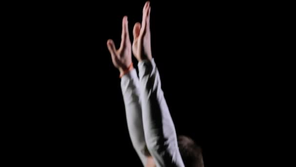 Вид збоку чоловіка в білому одязі на чорному тлі з'являється в рамці професійного акробата під час стрибка на батуті — стокове відео