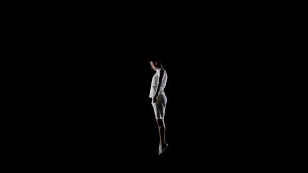 Красива чоловіча гімнастка в білому одязі на чорному тлі стрибає на батуті в повільному русі, виконуючи гвинти . — стокове відео