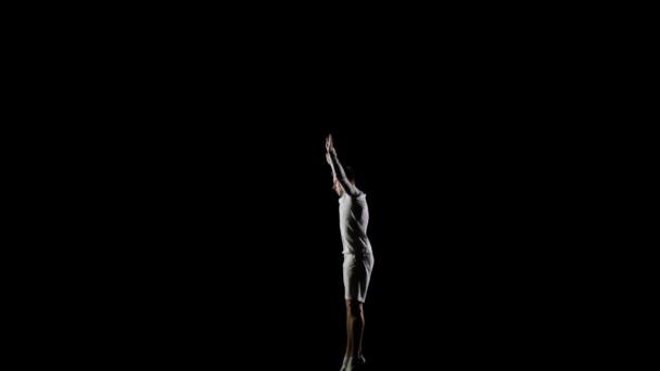 Beau gymnaste masculin en vêtements blancs sur un fond noir sautant sur une vue latérale du trampoline — Video