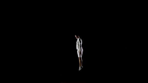 Όμορφος αρσενικό επαγγελματίας γυμναστής με λευκά ρούχα σε μαύρο φόντο εκτελεί στο διαγωνισμό γυμναστικής και εκτελεί ασκήσεις στο τραμπολίνο άλμα τούμπες. — Αρχείο Βίντεο