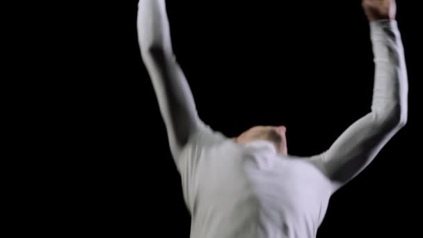 Молодой красивый акробат-гимнаст в белой одежде на черном фоне совершает прыжки и показывает трюки с вращением и сальто на батуте в замедленной съемке — стоковое видео