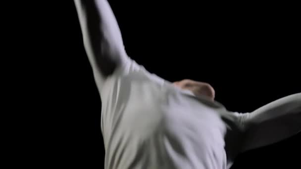 Красива чоловіча професійна гімнастка в білому одязі на чорному тлі виступає на змаганнях з гімнастики і виконує вправи на батуті, стрибаючи сорочками . — стокове відео