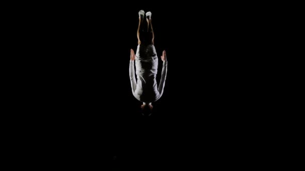 Atletisk man i vita kläder utför tricks hoppar på en studsmatta på svart monofoniska bakgrund — Stockvideo