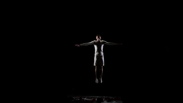 Siyah bir arka plan beyaz giysili Erkek jimnastikçi çerçeve içine aşağıdan soars ve havada dönme yapar ve ağır çekimde çevirir. Jimnastikçi rekabet. Bireysel beceri, uçuş ve — Stok video