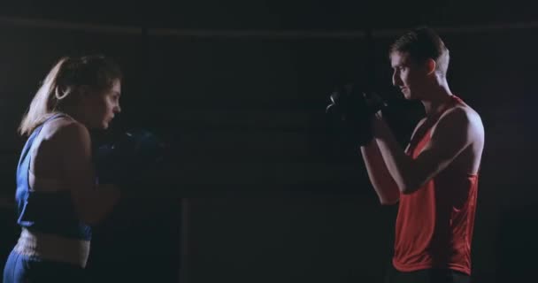 Vackra brunett boxare tränar slag mot tassarna med en tränare i ett mörkt rum — Stockvideo