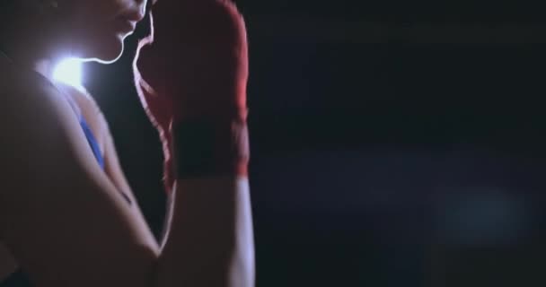 Una bella donna pugile si allena in una palestra buia e lavora pugni al rallentatore. vista laterale. Steadicam shot — Video Stock