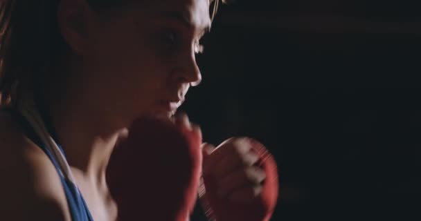 Een mooie vrouw bokser traint in een donkere sportschool en werkt stoten in slow motion. zijaanzicht. Steadicam schot — Stockvideo