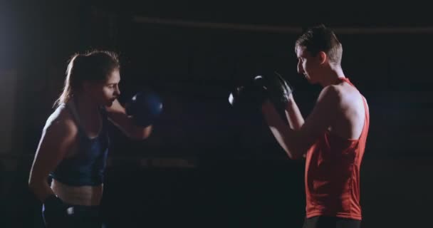 Hermosa boxeadora morena trabajando golpes en las patas con un entrenador en una habitación oscura — Vídeos de Stock