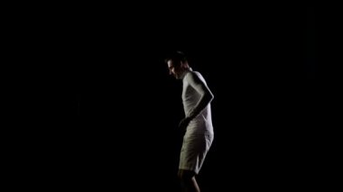 Atletik erkek Beyaz giysili bir trambolin tek sesli siyah bir arka plan üzerinde atlama hileler gerçekleştirir