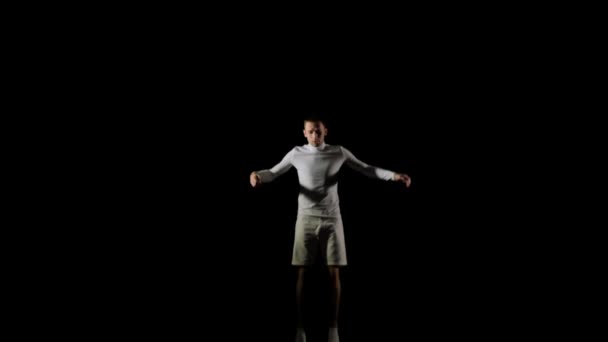 Человек в белом делает акробатику на черном фоне в замедленной съемке — стоковое видео