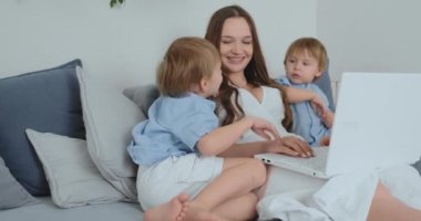 Anne bir dizüstü bilgisayar ile kanepede oturuyor. İki erkek çocuk şarkı ve kendi annemi benim için öp