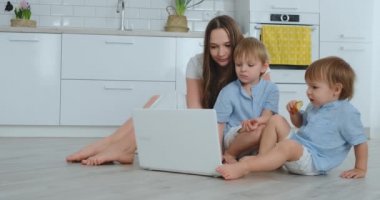 Modern Daire anne ve iki oğlu yerde oturma odasında otururken dizüstü bilgisayar ekranında bakın