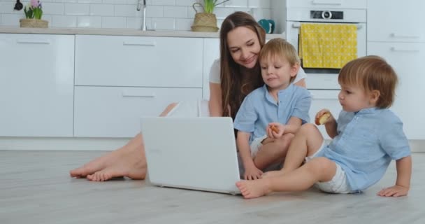 Modern technology. Modern apartment loving mom and two small sons sitting on the floor in the living room look at the laptop screen. Children with mom play on a laptop. — Stock Video