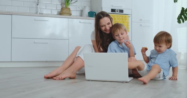 Moderni asunto rakastava äiti ja kaksi pientä poikaa istuu lattialla olohuoneessa katso kannettavan tietokoneen näytön. Lapset äidin kanssa leikkivät kannettavalla tietokoneella — kuvapankkivideo