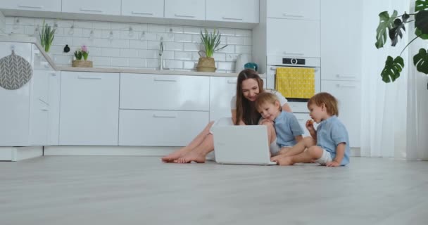 Bela família jovem moderna deitada no chão em casa e fazendo algo no laptop — Vídeo de Stock