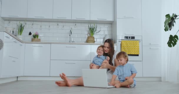 Moderne Technologie. Moderne Wohnung liebende Mutter und zwei kleine Söhne sitzen auf dem Boden im Wohnzimmer und schauen auf den Laptop-Bildschirm. Kinder mit Mama spielen am Laptop. — Stockvideo