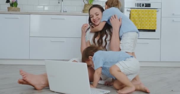 Mutter und zwei Kinder spielen auf dem Boden sitzend, umarmen sich und haben Spaß. eine glückliche Familie. das Spiel nach dem Betrachten des Laptops. Spiele mit Kindern. — Stockvideo
