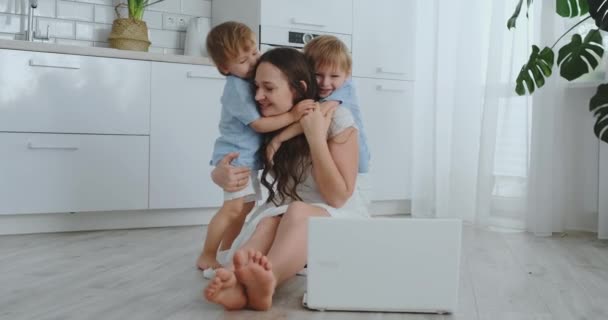 Madre e hijos cariñosos abrazándose y divirtiéndose jugando sentados en el suelo. Familia divertida y feliz. El juego después de ver el ordenador portátil — Vídeo de stock