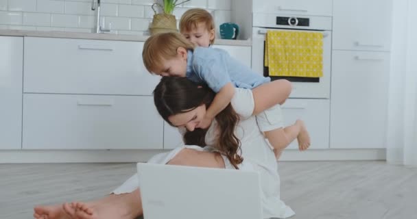 Mãe e duas crianças brincam sentadas no chão abraçando e se divertindo. Uma família feliz. O jogo depois de ver o laptop. Jogos com crianças . — Vídeo de Stock