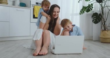 Modern Daire sevgi dolu anne ve oturma odasında katta oturan iki küçük oğlu dizüstü bilgisayar ekranında bakın. Çocuk anne ile bir dizüstü bilgisayarda oyun