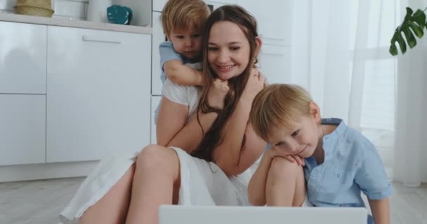 Anya és két gyermek ül a padlón átölelve, és a szórakozás. Egy boldog család. A játék után megtekintés a laptop. Gyerekjátékok. — Stock videók