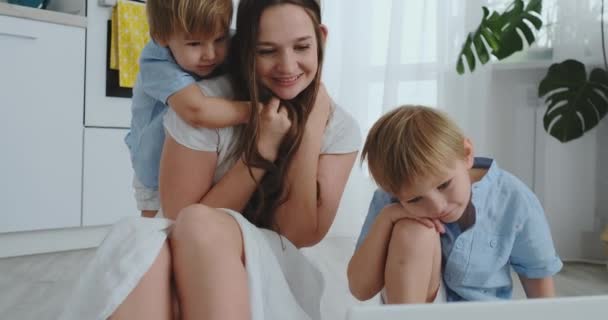 Amare mamma e bambini abbracciare e divertirsi giocando seduti sul pavimento. Famiglia divertente e felice. Il gioco dopo aver visto il computer portatile — Video Stock