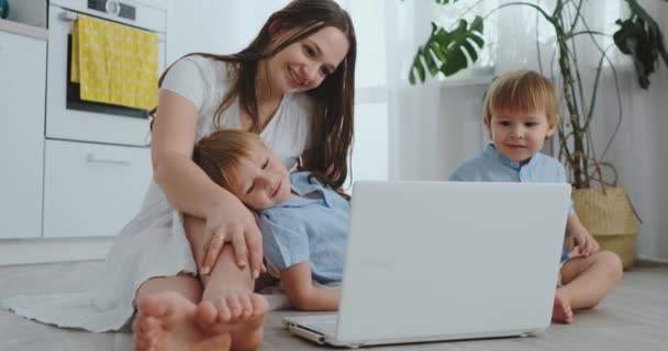 Moderno apartamento de mamá y dos hijos sentados en el suelo en la sala de estar mirar a la pantalla del ordenador portátil — Vídeos de Stock