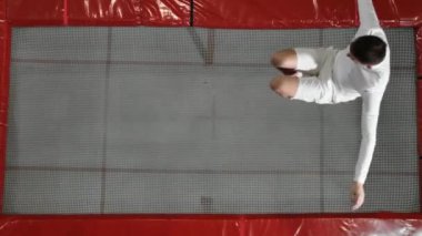 Beyaz kıyafetler içinde bir adam trambolin üst görünümünde atlama