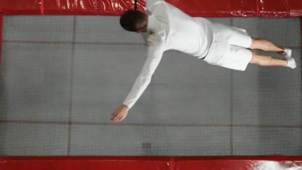 Вид с вершины гимнаста акробат в белом исполняет сальто на батуте — стоковое видео