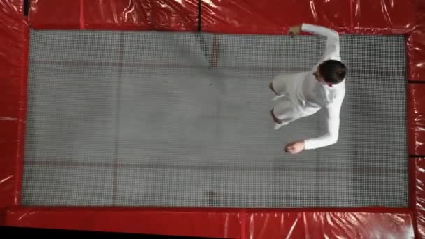 Top view gymnast acrobat in white clothes performs a somersault on a trampoline in slow motion — Stock Video